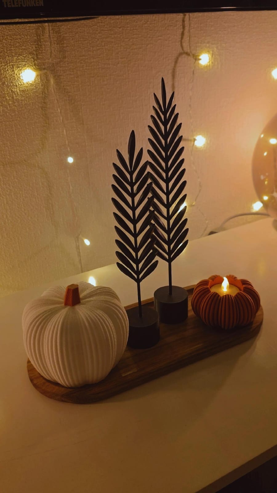 Herbst-Set mit Deko-Kürbis, zwei schwarzen Federn und beleuchtetem Kürbishalter auf einem Holzbrett.