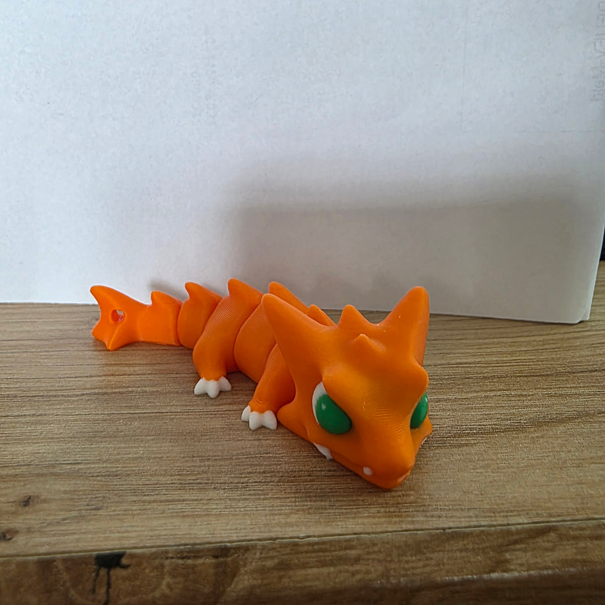 Orangefarbene Neobite-Figur mit grünen Augen auf einer Holzfläche.